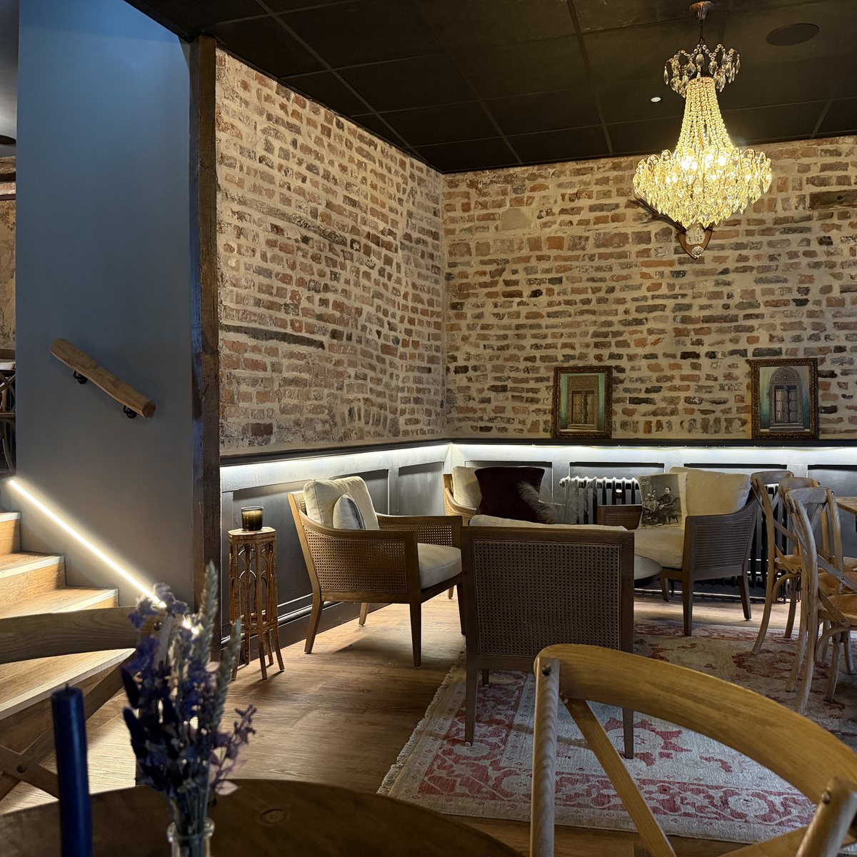 The main room — exposed brick, chandelier, banquette lighting and the lit stair